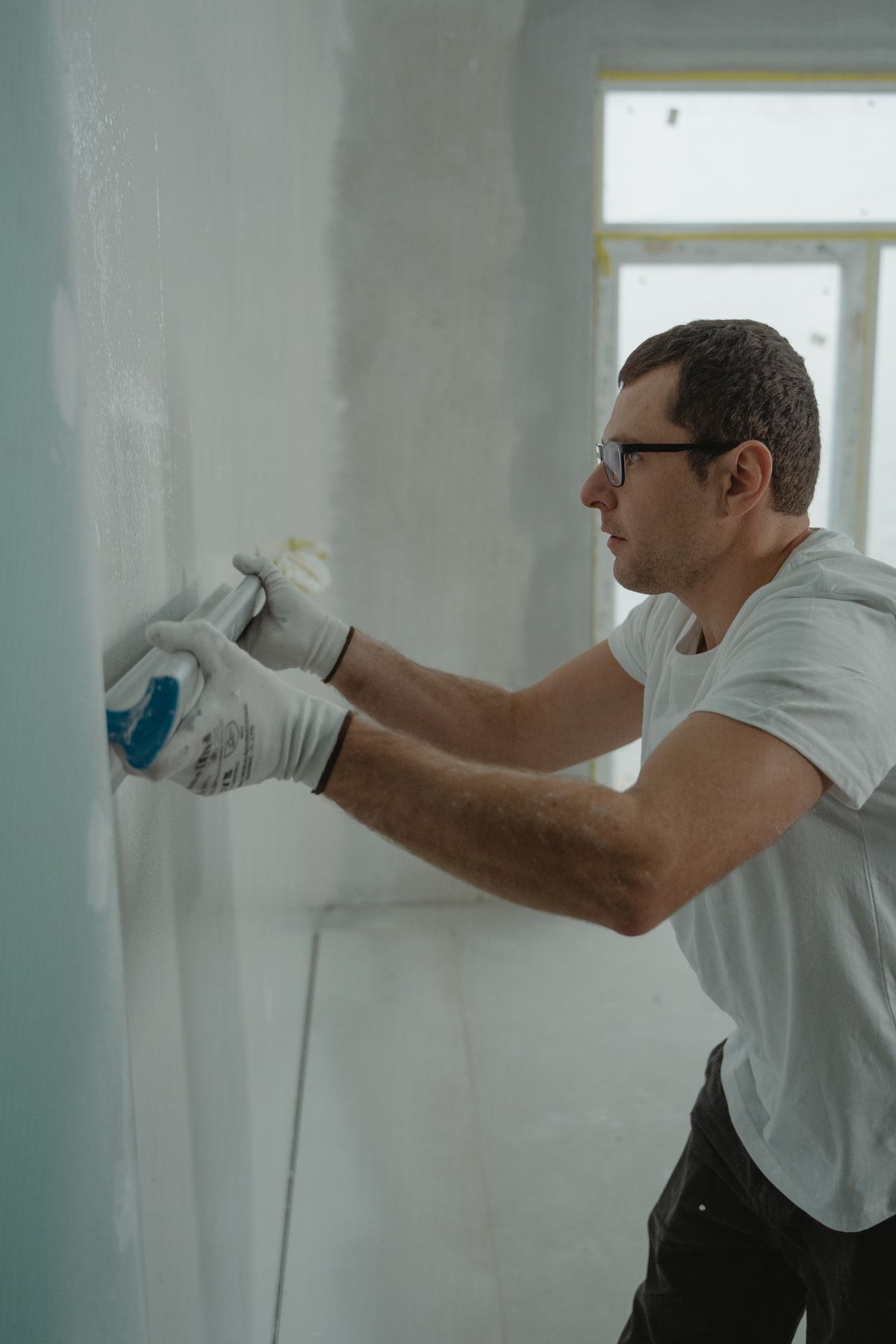 Finisher drawing joint compound across a wall with a taping knife during a skim-coat pass