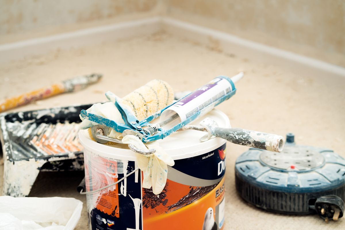 Paint bucket, roller sleeve, and tools staged on protected floors ahead of a ceiling repaint